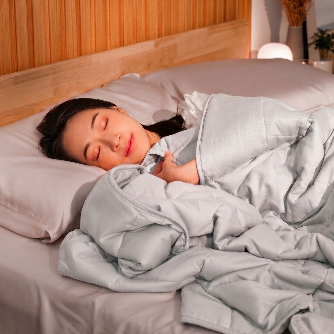Woman sleeping under a gray weighted blanket in a bedroom setting