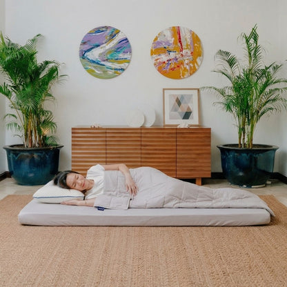 Person sleeping on a foldable mattress with Tencel bed sheets in a room with plants and wall art