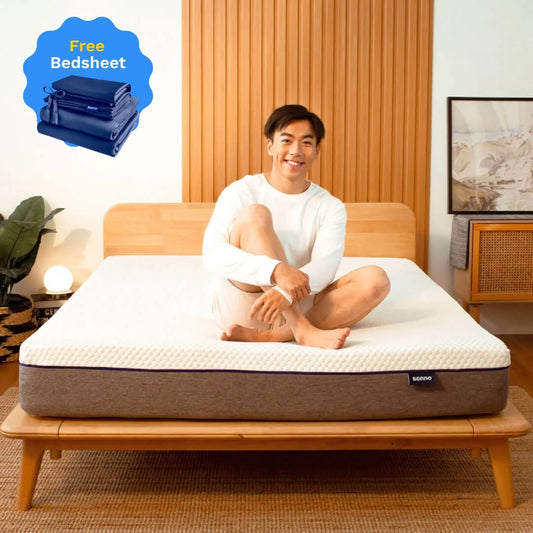 Person sitting on a mattress in a bedroom with a free bedsheet offer for Merdeka 2025.