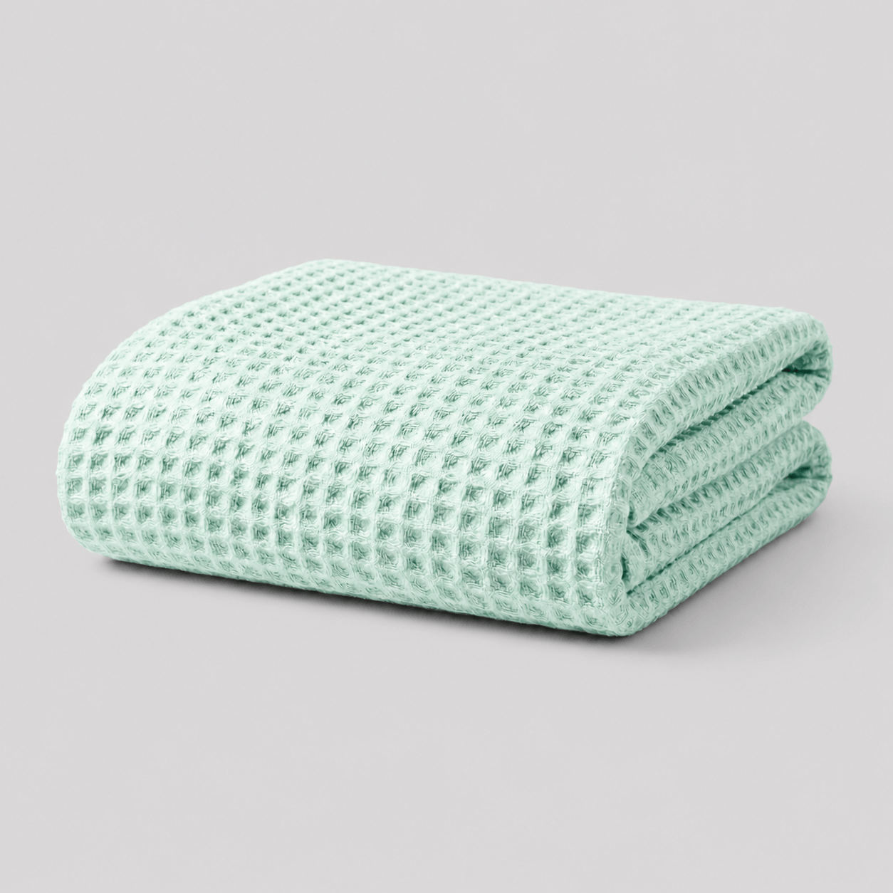 Folded mint green Sonno waffle-textured bamboo blanket on a light grey background