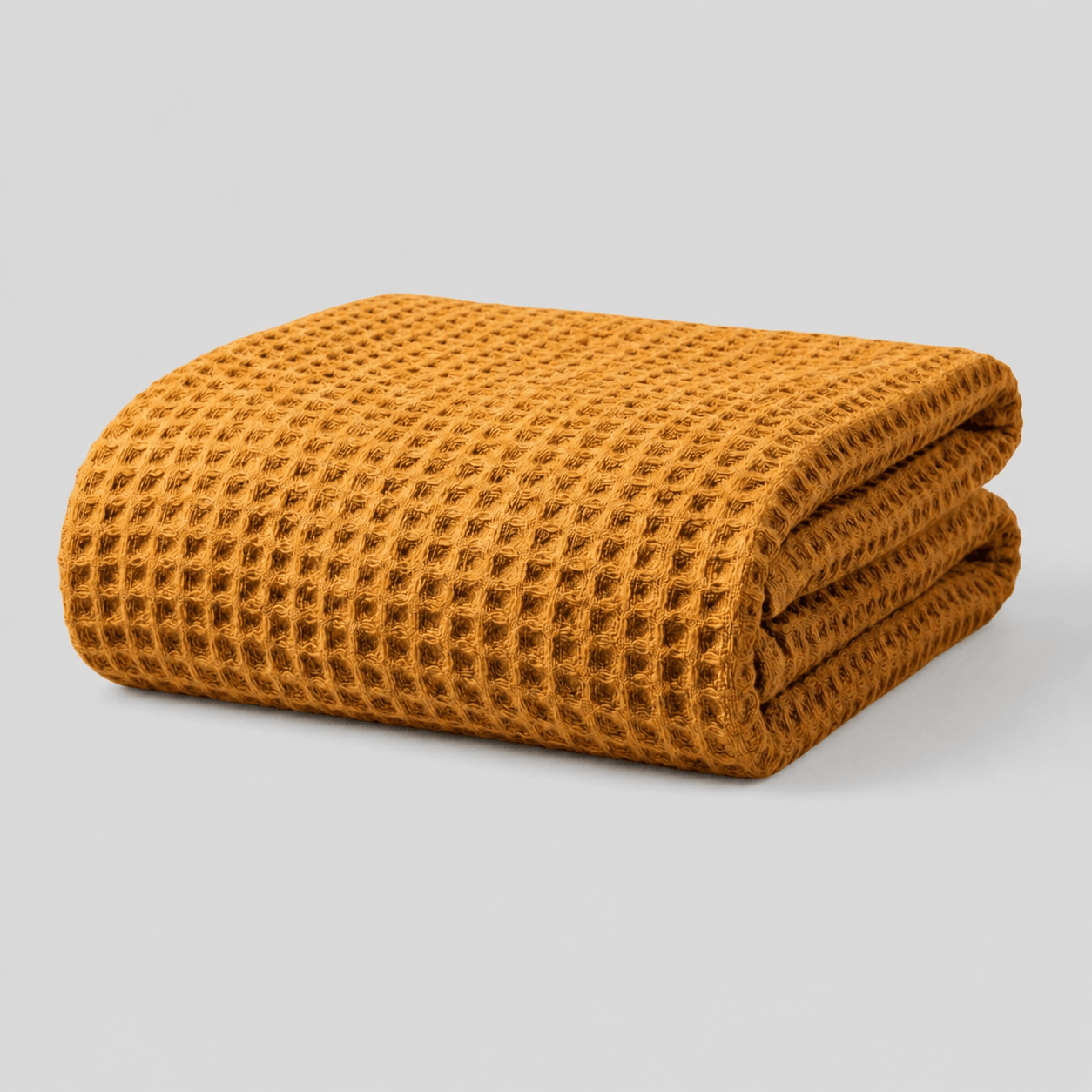 Folded mustard yellow Sonno waffle-textured blanket on a light grey background