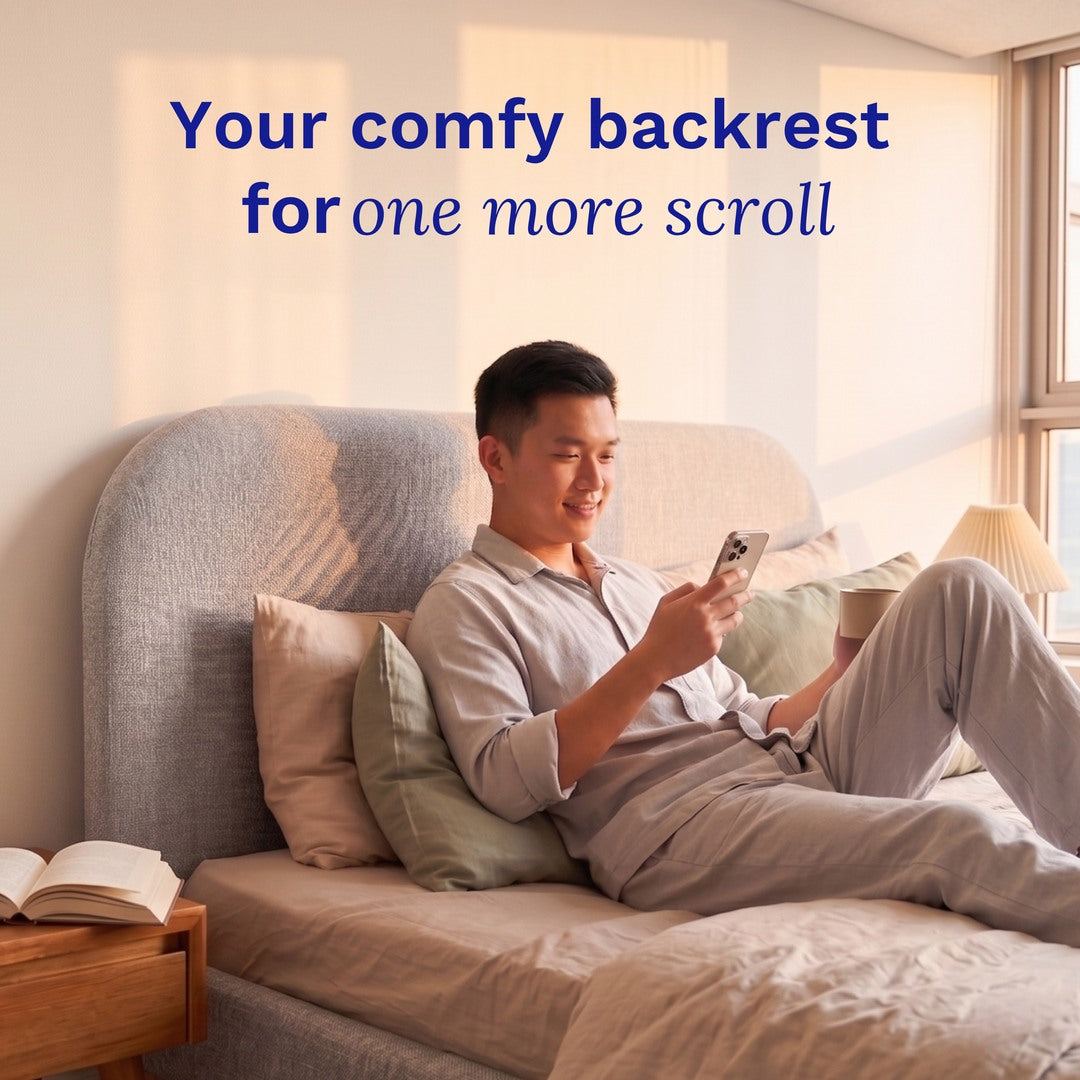 Man sitting on a Sonno Sunset Bed Frame  using a smartphone with text 'Your comfy backrest for one more scroll' in a bright room.