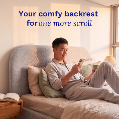 Man sitting on a Sonno Sunset Bed Frame  using a smartphone with text 'Your comfy backrest for one more scroll' in a bright room.