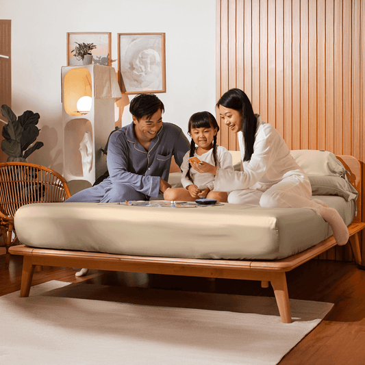 A family enjoying quality time together on a Sonno bed, with a cozy atmosphere. The parents are sitting with their daughter, engaging in an activity, surrounded by stylish decor, highlighting a warm and inviting bedroom environment.