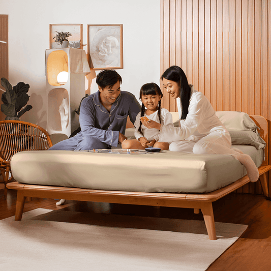 A family enjoying quality time together on a Sonno bed, with a cozy atmosphere. The parents are sitting with their daughter, engaging in an activity, surrounded by stylish decor, highlighting a warm and inviting bedroom environment.